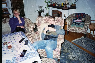 Vintage living room scene with two individuals in mid-1990s/early 2000s décor. Woman in blue sweater rests on floral-patterne...