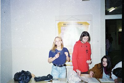 Vintage indoor scene featuring three individuals in casual 1990s attire—blue polo, red hoodie, and brown jacket—engaged in a ...