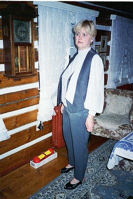 Vintage interior featuring a woman in a 1970s-style blazer and high-waisted trousers, posing beside a wooden-framed clock and...