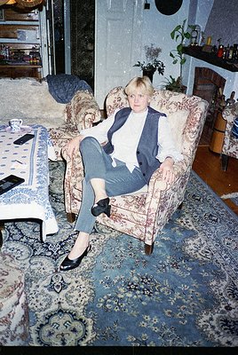Vintage interior portrait of a woman in a relaxed pose on a floral-patterned armchair, wearing a blazer over a white top, hig...