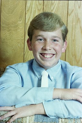 Portrait of a young man in a light blue dress shirt and striped tie, leaning on a wooden-paneled wall. Mid-20th century forma...