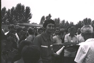 Vintage black-and-white photo of a crowded outdoor gathering, likely a public event or rally. Central figure in a striped shi...