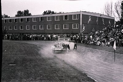 Vintage black-and-white photo of a classic car race on a wet track, 1950s. A vintage convertible (likely a pre-war model) spe...