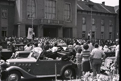 Black-and-white street scene featuring a large crowd gathered around a grand, neoclassical building with arched windows and a...