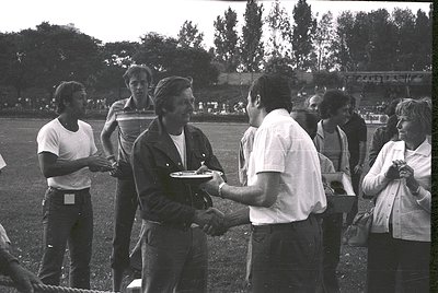 Handshake ceremony on grassy field with blurred stadium in background. Mid-20th century sports event, likely 1960s–1970s. Win...