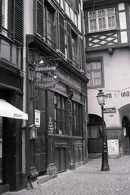 Historic Strasbourg timber-framed building with "Kronenbourg" beer signage, cobblestone street, and vintage street lamp.