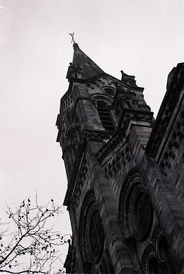 Gothic Revival-style church tower with pointed spire, intricate stone carvings, and arched buttresses. Architectural details ...