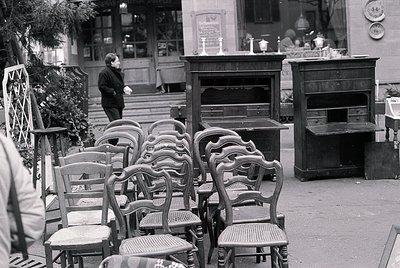 Vintage outdoor café seating with ornate wooden chairs and tables, likely from the 1950s–1970s. Antique display cabinets and ...