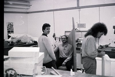 Architectural studio workspace with three professionals reviewing model and plans, 1970s-1980s. Wooden models, drafting table...