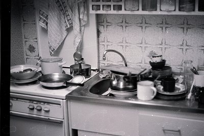 Mid-century kitchen with vintage stove, sink, and countertop cluttered with dishes, a teapot, and a coffee maker. Geometric w...
