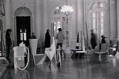 Elegant 1960s–70s interior featuring geometric modernist furniture and grand classical architecture. White plastic chairs and...