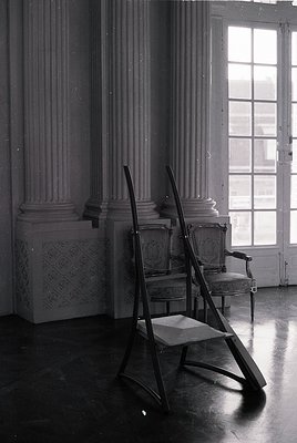 Neoclassical interior featuring tall fluted columns with ornate capitals. Two vintage chairs with curved wooden frames and pa...