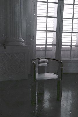 Minimalist interior featuring a single modernist chair with black metal frame and white seat, positioned in a dimly lit room ...