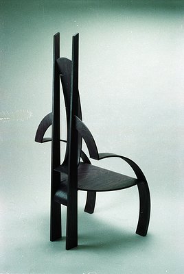 Mid-century modern chair with organic, sculptural wood design—curved backrest, tapered legs, and minimalist armrests. Likely ...