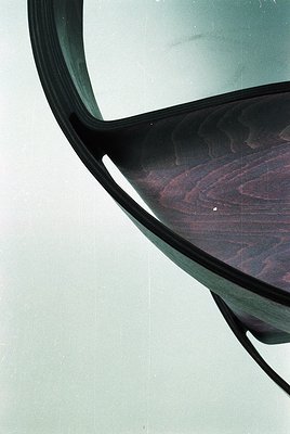 Mid-century modern chair with curved wooden seat and black metal frame, showcasing organic design. Reflective surface capture...