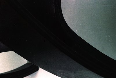Close-up of a vintage car’s curved windshield and side mirror, showing subtle scratches and minor water spots. Reflects muted...
