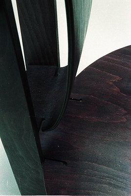 Mid-century modern chair leg with tapered, curved metal frame and dark wood seat—minimalist design. Likely 1950s–1970s indust...