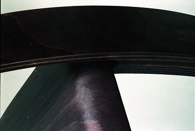 Close-up of a sleek, curved wooden chair leg with smooth, dark finish—likely mid-century modern design. The polished grain an...