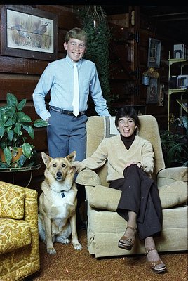 A mid-20th-century indoor portrait featuring a man in a light blue dress shirt and tie standing beside a woman in a beige bla...