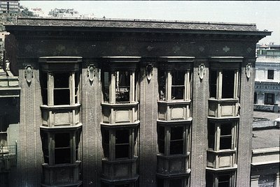 Neoclassical brick building facade featuring four symmetrical bay windows with decorative stone trim and corbels. Flat roof w...