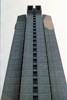 Tall, Brutalist-style concrete tower with vertical slit windows and minimalist design, likely from the 1960s–1980s. Symmetric...