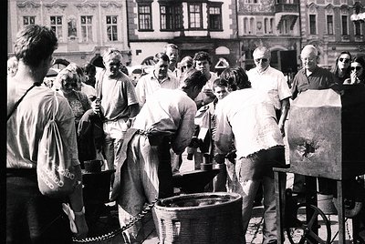 Group of people gathered around a large, open cooking pot in an urban courtyard, likely preparing a communal meal. Architectu...