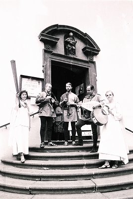 Vintage black-and-white photo of a folk ensemble performing at a church entrance, likely Eastern European . Group includes mu...