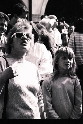 Black-and-white candid of two women in mid-20th-century streetwear—adult in sleeveless top, sunglasses, and a crossbody bag; ...