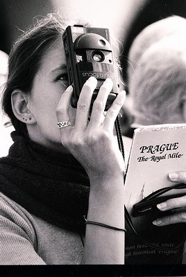 Vintage black-and-white photo of a woman holding a **Sony Mavica** camera (1980s model) while reading *"Prague: The Royal Mil...