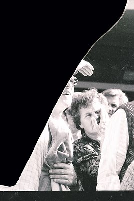 Black-and-white candid of elderly woman in patterned sweater adjusting her hair, framed by a dark car’s rearview mirror. Mid-...