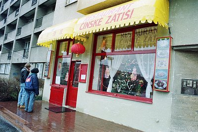 Vintage Chinese restaurant "Čínské Zápisí" in a Soviet-era building, featuring red doors, yellow awnings, and red lanterns. D...