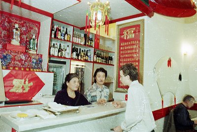 Vintage interior of a Chinese restaurant or teahouse, featuring red lacquered walls, shelves stocked with bottled drinks, and...