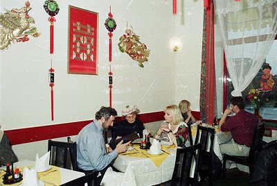 Vintage Asian-themed restaurant interior with red-and-gold decor, featuring dragon and shield wall hangings. Four adults seat...