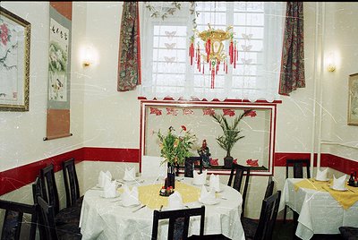 Vintage-style restaurant interior with ornate Asian-inspired decor. Round tables set with white tablecloths, folded napkins, ...