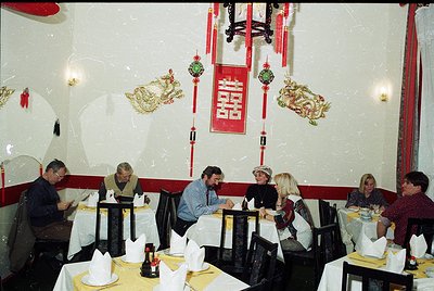 Mid-century Asian-themed restaurant interior with red-and-gold dragon motifs and calligraphy. Round tables, black chairs, and...