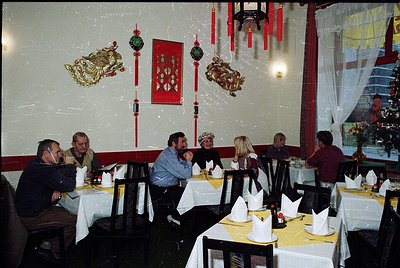 Vintage restaurant interior with Asian-inspired decor: round tables draped in white tablecloths, red lanterns, and gold drago...