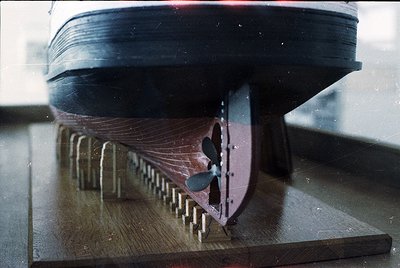 Close-up of a vintage ship propeller mounted on a wooden display stand, showcasing intricate blade details and rivets. Likely...