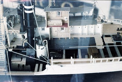 Miniature model of a mid-20th century industrial ship, featuring a smokestack, lifeboat, and deck machinery. The structure in...