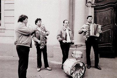Street quartet in 1970s Eastern Bloc urban setting. Four musicians—saxophonist, accordionist, drummer, and saxophonist—perfor...