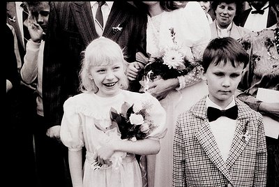 Young girl and boy in formal attire, likely 1950s–1970s Western/European wedding. Girl wears a simple white dress with bouque...