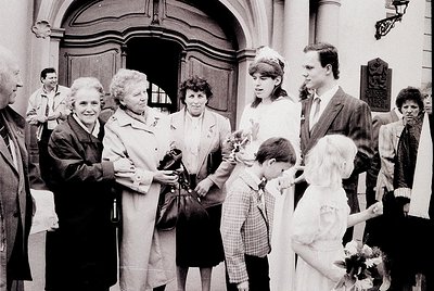 Black-and-white photo of a wedding procession outside a grand, arched doorway, likely Eastern European . Six adults in formal...