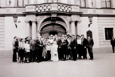 Neoclassical building entrance with arched doorway and decorative lanterns, hosting a 1970s wedding group shot. Bride in whit...