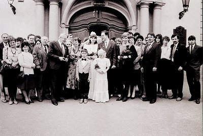 Group wedding photo in grand neoclassical building entrance, likely Eastern Bloc era (1970s–1980s). Bride in simple white gow...