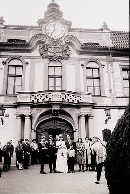 Neoclassical building facade featuring a prominent clock tower and arched entrance, flanked by columns. A wedding party stand...