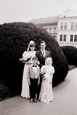 Family portrait featuring a bride in a full-length white gown with floral bouquet, groom in a dark suit, and two children in ...