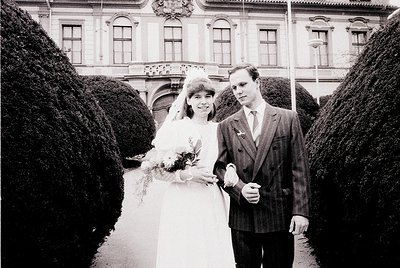 1970s black-and-white wedding portrait in European classical courtyard. Bride in full-length gown with bouquet, groom in pins...