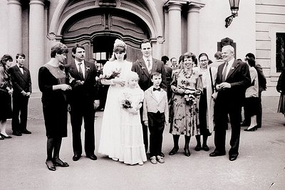 Neoclassical building entrance with arched doorway, featuring a 1970s wedding group portrait. Bride in full-length gown with ...