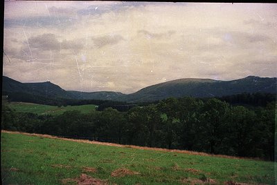 Vintage landscape shot of rolling hills and dense forest under overcast skies. The faded sepia tone suggests mid-20th century...