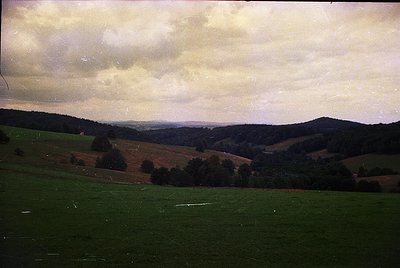 Vintage landscape shot of rolling hills and pastures under overcast skies, likely mid-20th century. Distinctive patchwork fie...