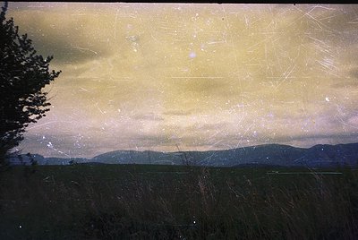 Vintage sepia-toned landscape shot through scratched film, revealing layered mountain ranges under overcast skies. Distorted ...